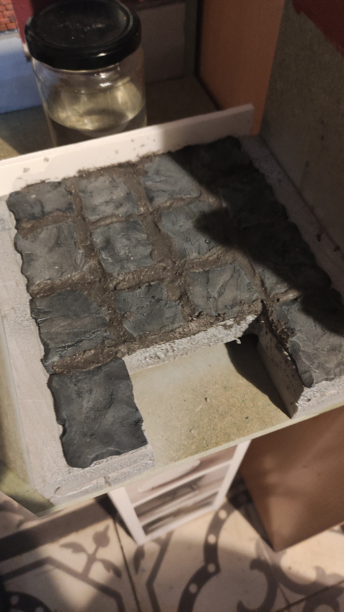 Diorama artesanal de Venecia durante la peste negra, mostrando a dos médicos de la peste con máscara frente a una góndola en un canal, con iluminación de farol.