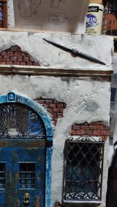 Diorama artesanal de Venecia durante la peste negra, mostrando a dos médicos de la peste con máscara frente a una góndola en un canal, con iluminación de farol.