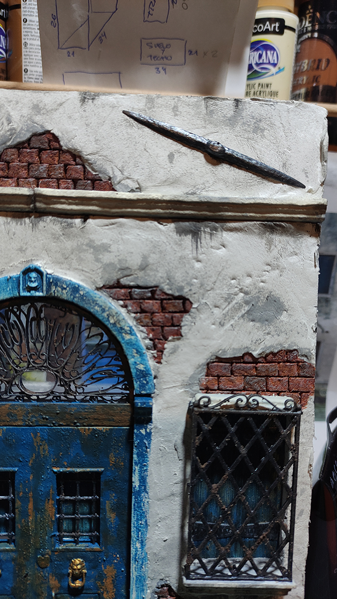 Diorama artesanal de Venecia durante la peste negra, mostrando a dos médicos de la peste con máscara frente a una góndola en un canal, con iluminación de farol.