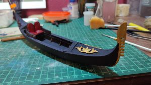 Diorama artesanal de Venecia durante la peste negra, mostrando a dos médicos de la peste con máscara frente a una góndola en un canal, con iluminación de farol.