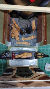 Diorama artesanal de Venecia durante la peste negra, mostrando a dos médicos de la peste con máscara frente a una góndola en un canal, con iluminación de farol.