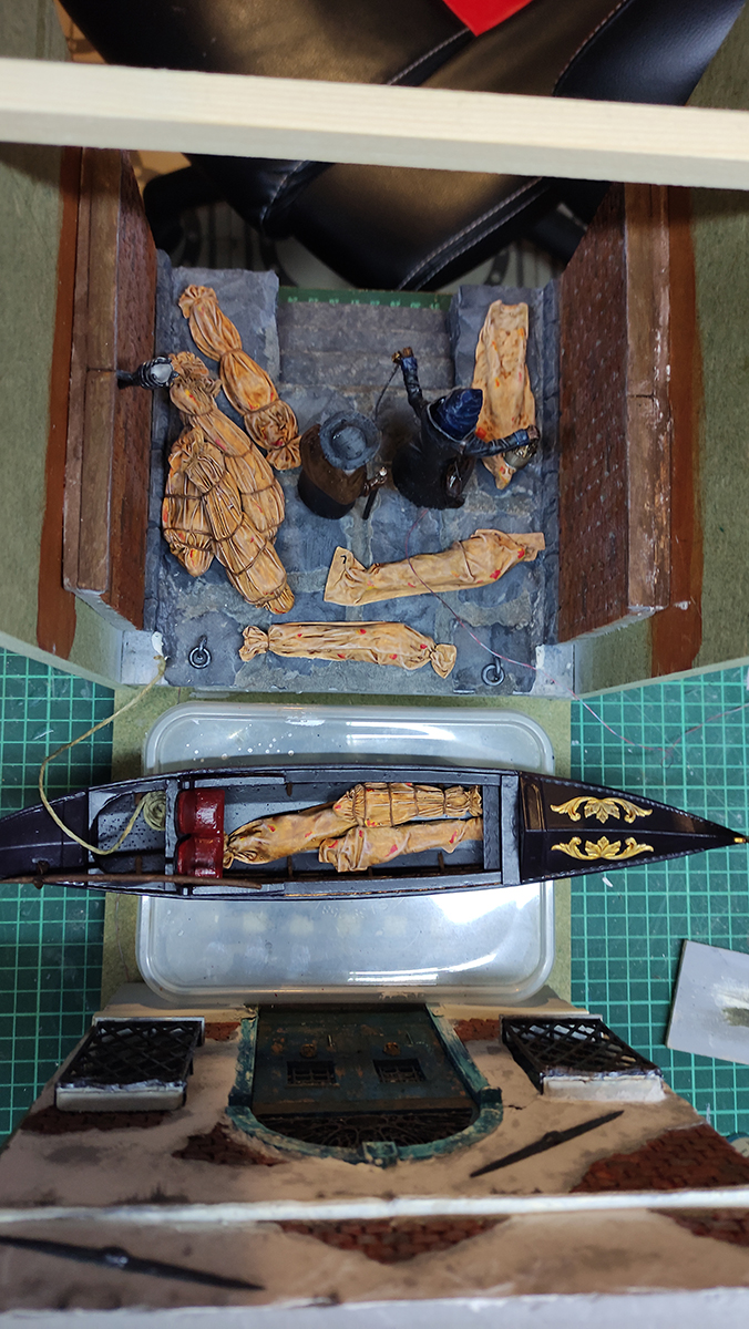 Diorama artesanal de Venecia durante la peste negra, mostrando a dos médicos de la peste con máscara frente a una góndola en un canal, con iluminación de farol.