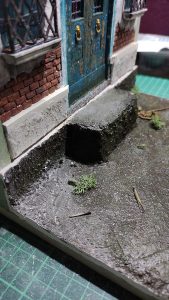 Diorama artesanal de Venecia durante la peste negra, mostrando a dos médicos de la peste con máscara frente a una góndola en un canal, con iluminación de farol.