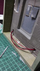 Diorama artesanal de Venecia durante la peste negra, mostrando a dos médicos de la peste con máscara frente a una góndola en un canal, con iluminación de farol.