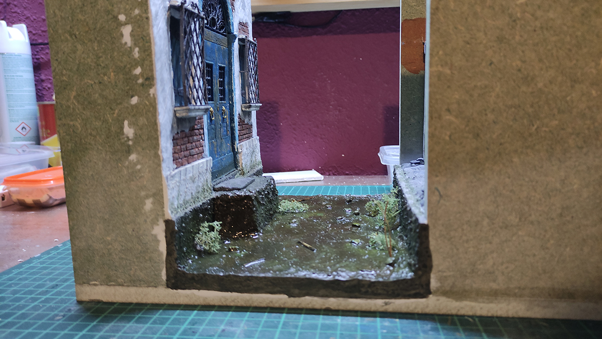 Diorama artesanal de Venecia durante la peste negra, mostrando a dos médicos de la peste con máscara frente a una góndola en un canal, con iluminación de farol.