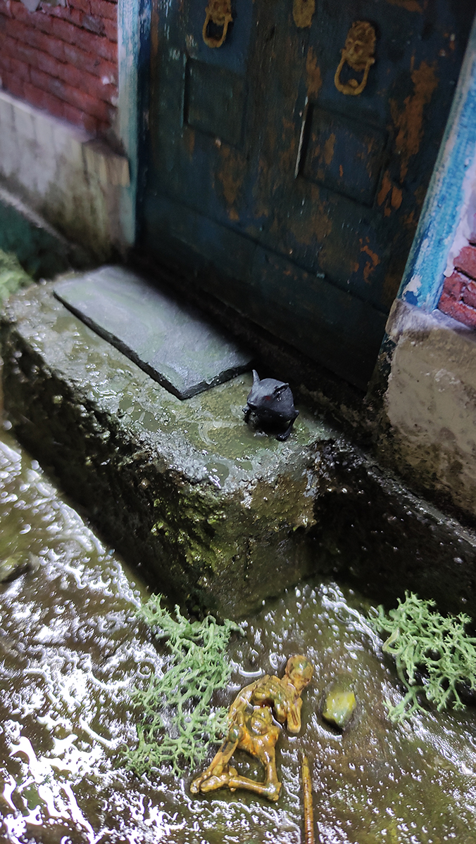 Diorama artesanal de Venecia durante la peste negra, mostrando a dos médicos de la peste con máscara frente a una góndola en un canal, con iluminación de farol.