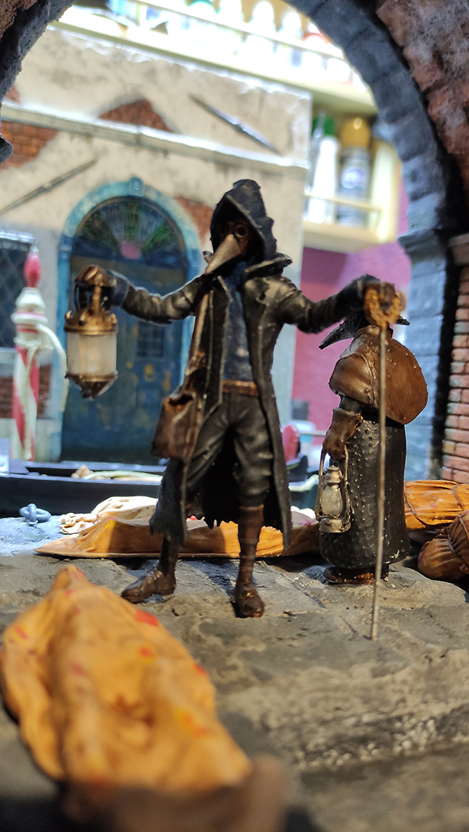 Diorama artesanal de Venecia durante la peste negra, mostrando a dos médicos de la peste con máscara frente a una góndola en un canal, con iluminación de farol.