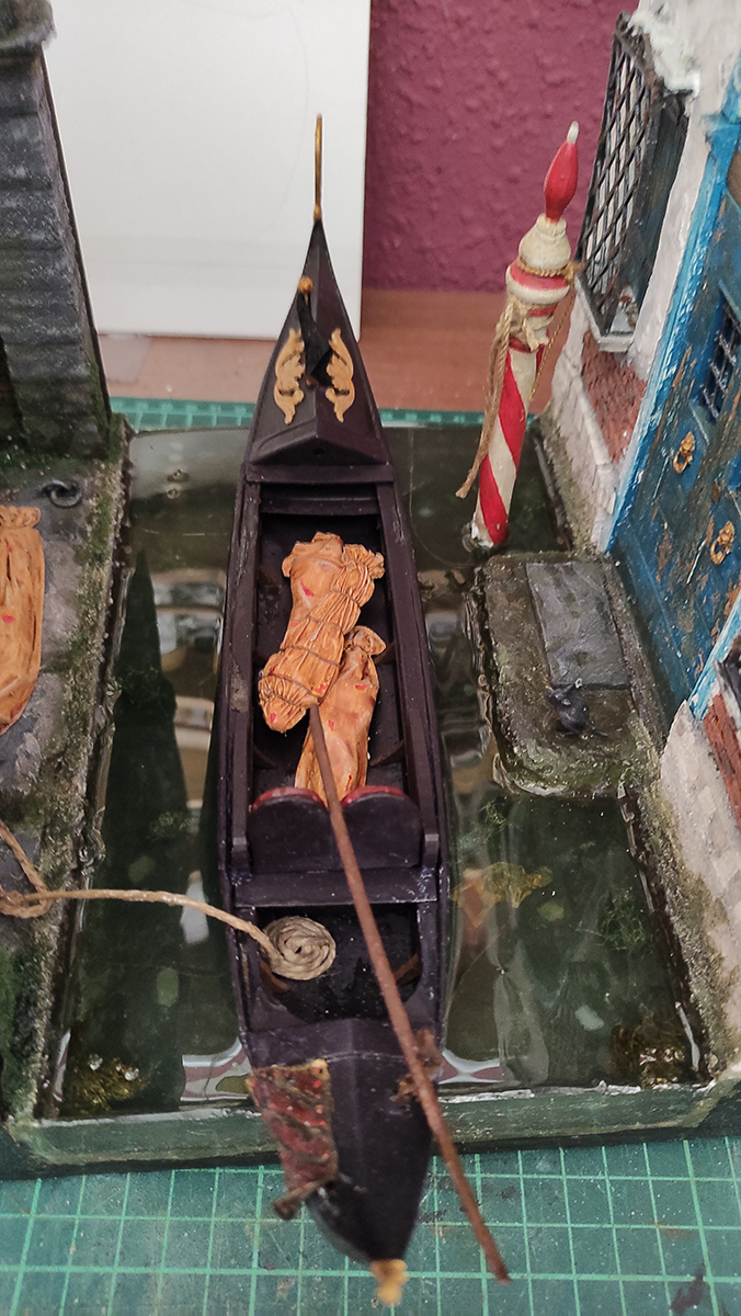 Diorama artesanal de Venecia durante la peste negra, mostrando a dos médicos de la peste con máscara frente a una góndola en un canal, con iluminación de farol.
