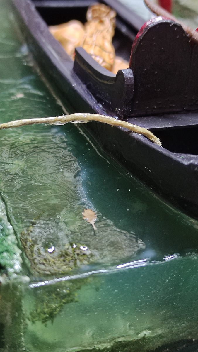 Diorama artesanal de Venecia durante la peste negra, mostrando a dos médicos de la peste con máscara frente a una góndola en un canal, con iluminación de farol.