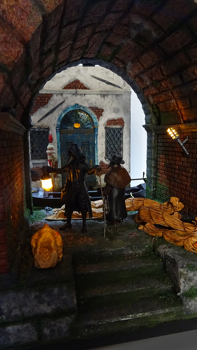 Diorama artesanal de Venecia durante la peste negra, mostrando a dos médicos de la peste con máscara frente a una góndola en un canal, con iluminación de farol.