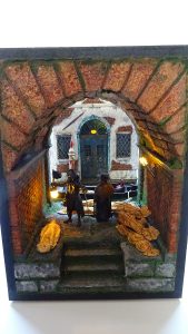 Diorama artesanal de Venecia durante la peste negra, mostrando a dos médicos de la peste con máscara frente a una góndola en un canal, con iluminación de farol.