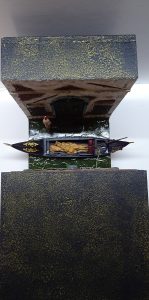 Diorama artesanal de Venecia durante la peste negra, mostrando a dos médicos de la peste con máscara frente a una góndola en un canal, con iluminación de farol.