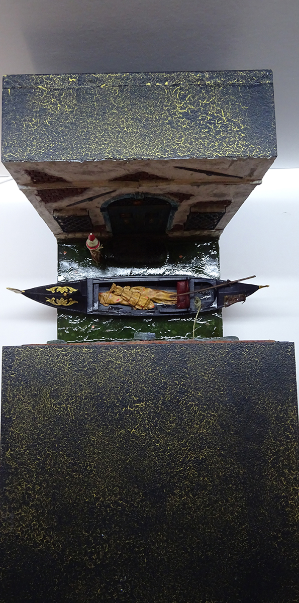 Diorama artesanal de Venecia durante la peste negra, mostrando a dos médicos de la peste con máscara frente a una góndola en un canal, con iluminación de farol.