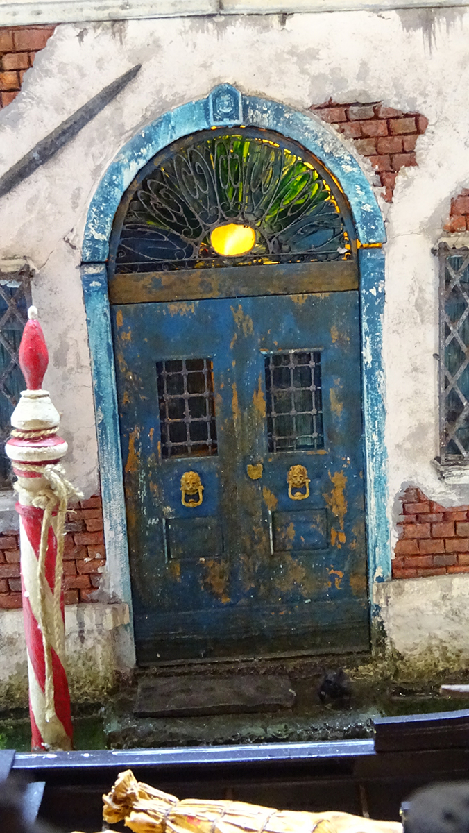 Diorama artesanal de Venecia durante la peste negra, mostrando a dos médicos de la peste con máscara frente a una góndola en un canal, con iluminación de farol.