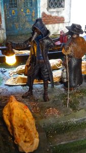 Diorama artesanal de Venecia durante la peste negra, mostrando a dos médicos de la peste con máscara frente a una góndola en un canal, con iluminación de farol.