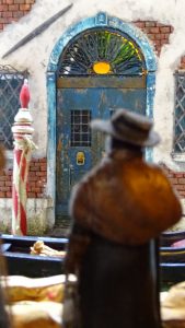 Diorama artesanal de Venecia durante la peste negra, mostrando a dos médicos de la peste con máscara frente a una góndola en un canal, con iluminación de farol.