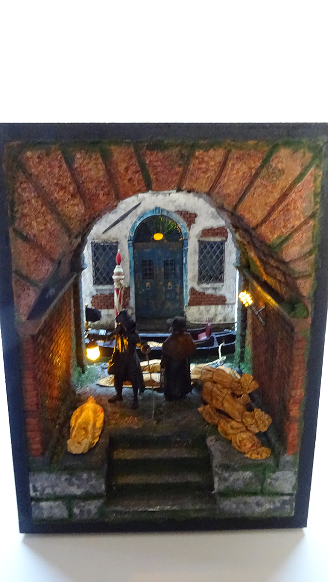 Diorama artesanal de Venecia durante la peste negra, mostrando a dos médicos de la peste con máscara frente a una góndola en un canal, con iluminación de farol.