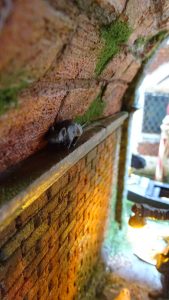 Diorama artesanal de Venecia durante la peste negra, mostrando a dos médicos de la peste con máscara frente a una góndola en un canal, con iluminación de farol.
