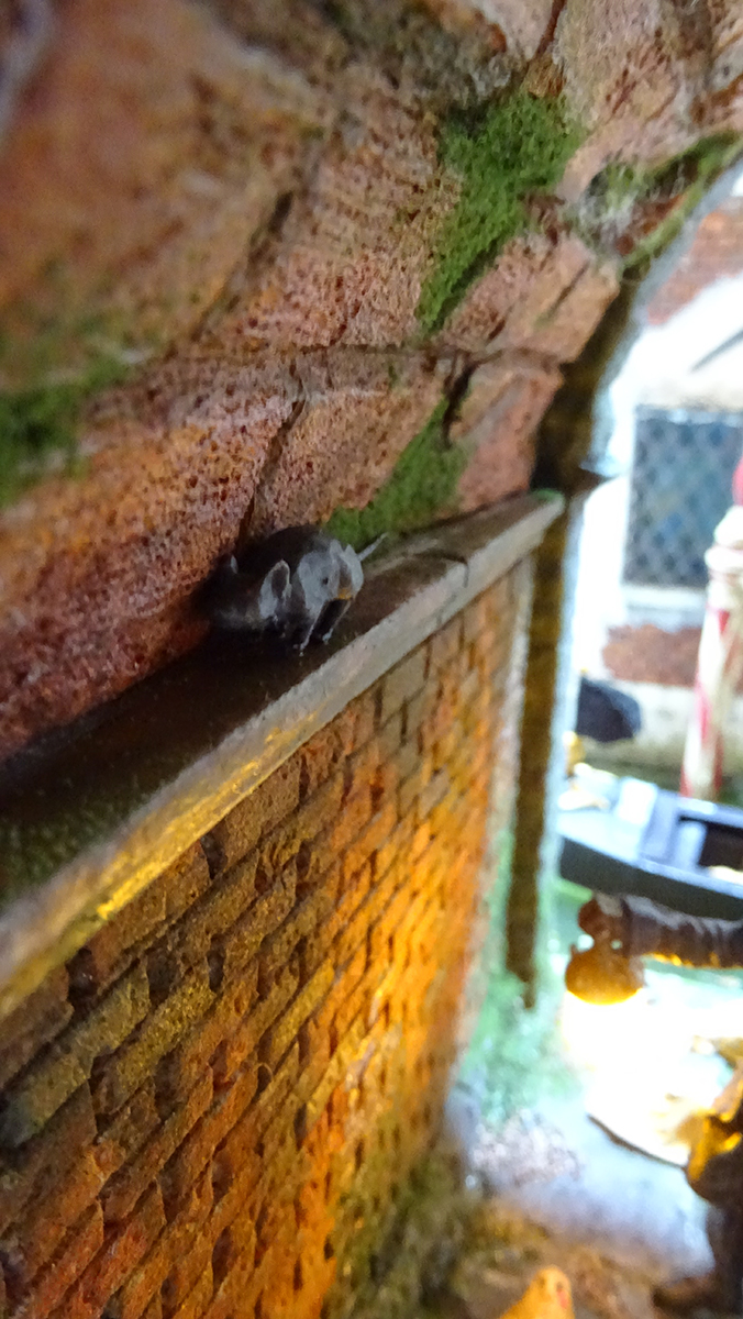 Diorama artesanal de Venecia durante la peste negra, mostrando a dos médicos de la peste con máscara frente a una góndola en un canal, con iluminación de farol.