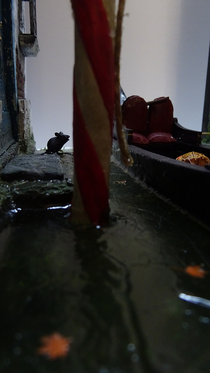 Diorama artesanal de Venecia durante la peste negra, mostrando a dos médicos de la peste con máscara frente a una góndola en un canal, con iluminación de farol.