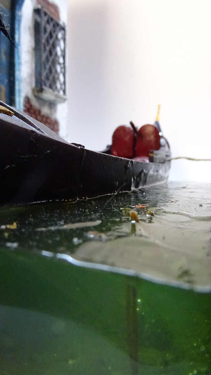 Diorama artesanal de Venecia durante la peste negra, mostrando a dos médicos de la peste con máscara frente a una góndola en un canal, con iluminación de farol.