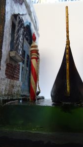 Diorama artesanal de Venecia durante la peste negra, mostrando a dos médicos de la peste con máscara frente a una góndola en un canal, con iluminación de farol.