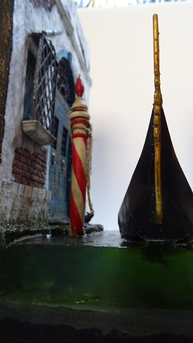 Diorama artesanal de Venecia durante la peste negra, mostrando a dos médicos de la peste con máscara frente a una góndola en un canal, con iluminación de farol.