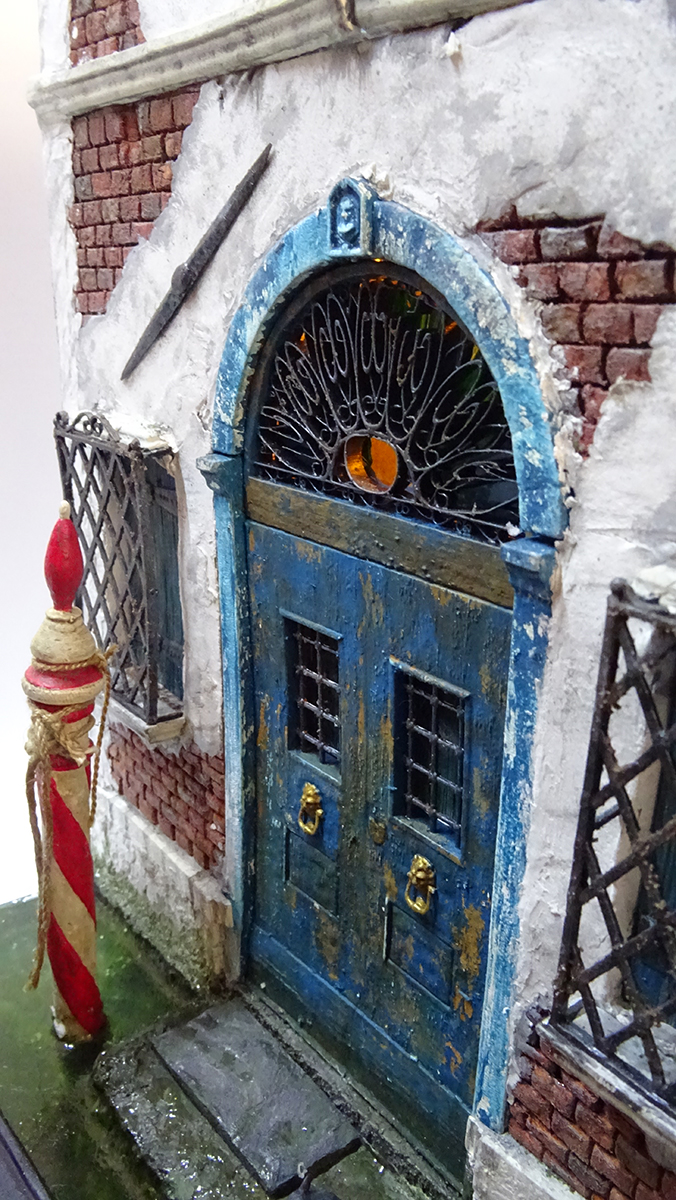 Diorama artesanal de Venecia durante la peste negra, mostrando a dos médicos de la peste con máscara frente a una góndola en un canal, con iluminación de farol.