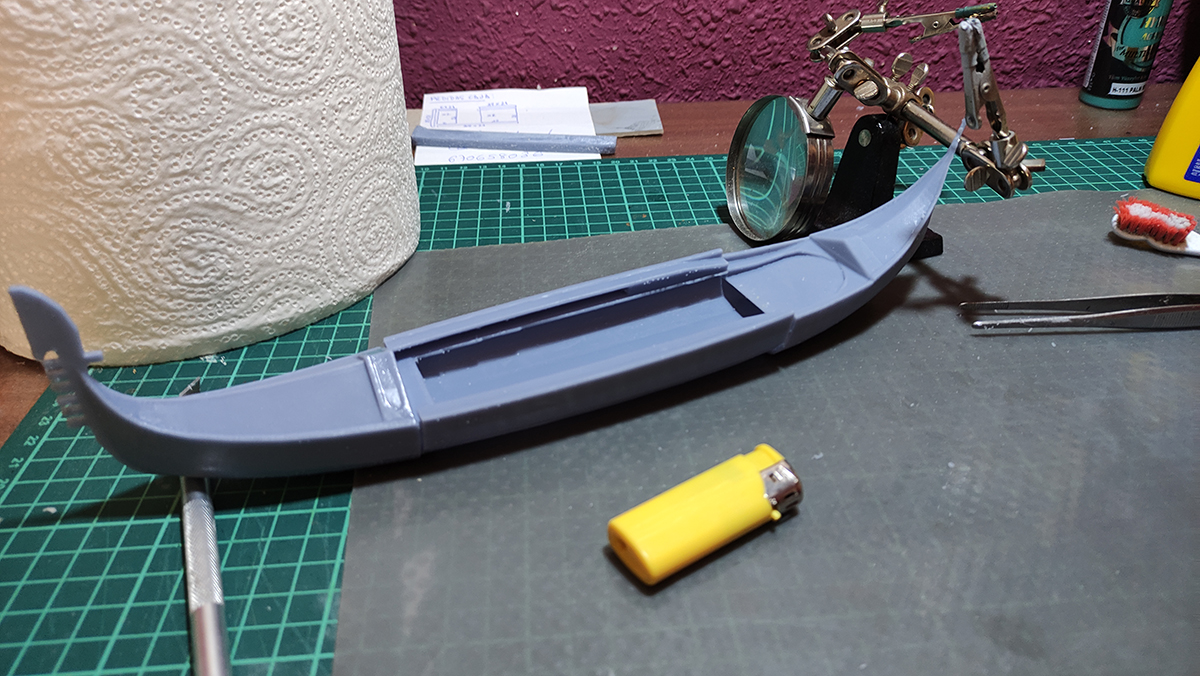 Diorama artesanal de Venecia durante la peste negra, mostrando a dos médicos de la peste con máscara frente a una góndola en un canal, con iluminación de farol.