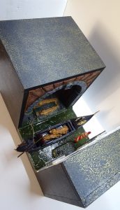 Vista superior del diorama de Venecia con góndola y cuerpos envueltos en mortajas, mostrando el acabado exterior artístico y la estructura del book nook.