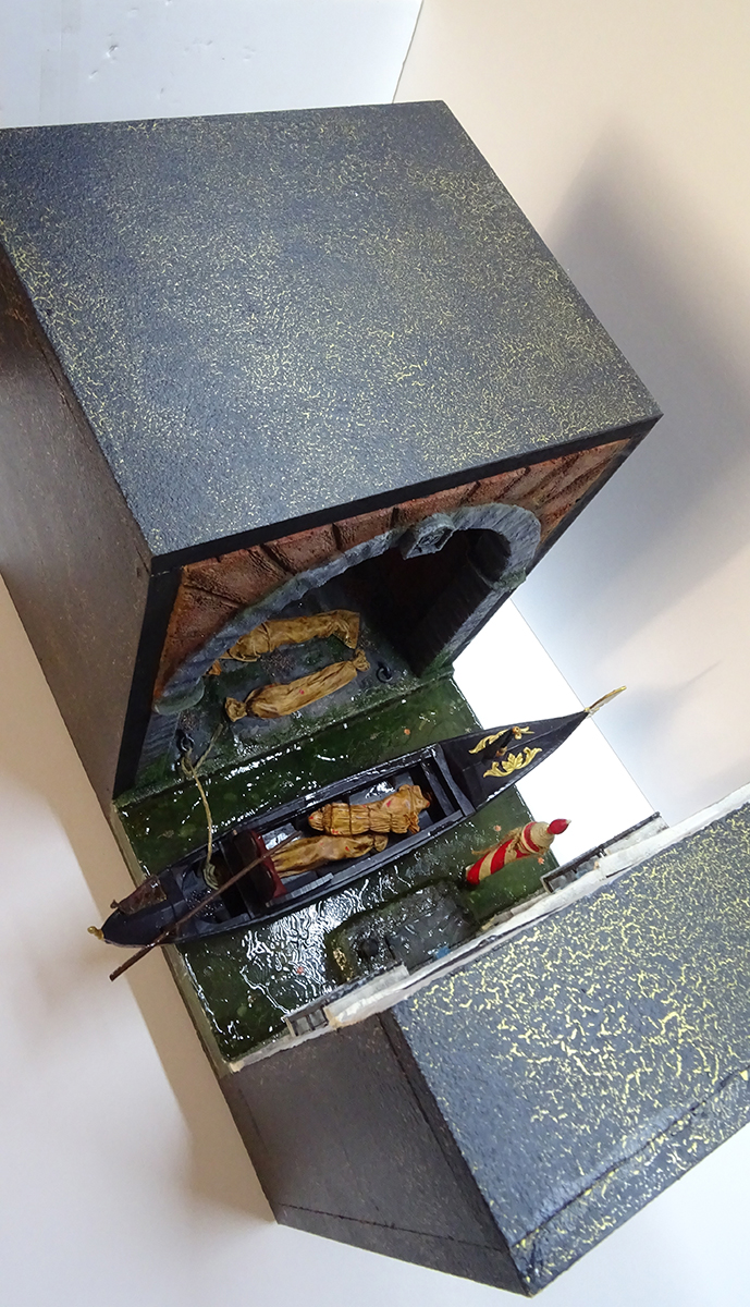 Vista superior del diorama de Venecia con góndola y cuerpos envueltos en mortajas, mostrando el acabado exterior artístico y la estructura del book nook.