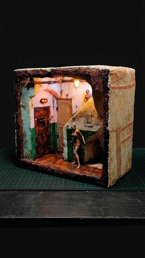 Diorama artesanal de Silent Hill tipo Book Nook, con la enfermera (Bubble Head Nurse) en un pasillo de hospital oxidado e iluminación LED tenue.