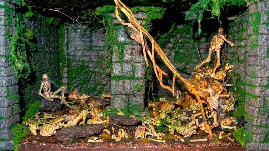 Primer plano del interior del diorama de la Inquisición, mostrando una mazmorra subterránea con un pilar central y una fosa común repleta de esqueletos artesanales.