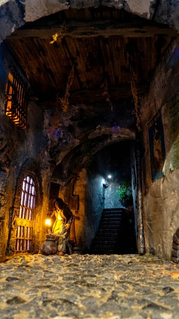 Diorama del Sacamantecas en un callejón oscuro con adoquines, iluminación de farol real y escaleras al fondo.