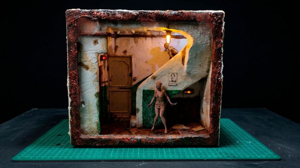 Diorama artesanal de Silent Hill tipo Book Nook, con la enfermera (Bubble Head Nurse) en un pasillo de hospital oxidado e iluminación LED tenue.
