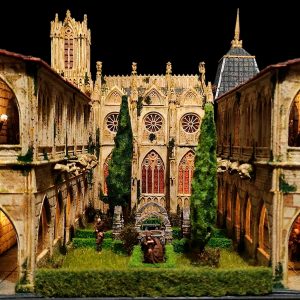 Diorama artesanal de arquitectura gótica medieval con catedral iluminada, figuras de monjes y vegetación natural a escala, obra de 27dioramas